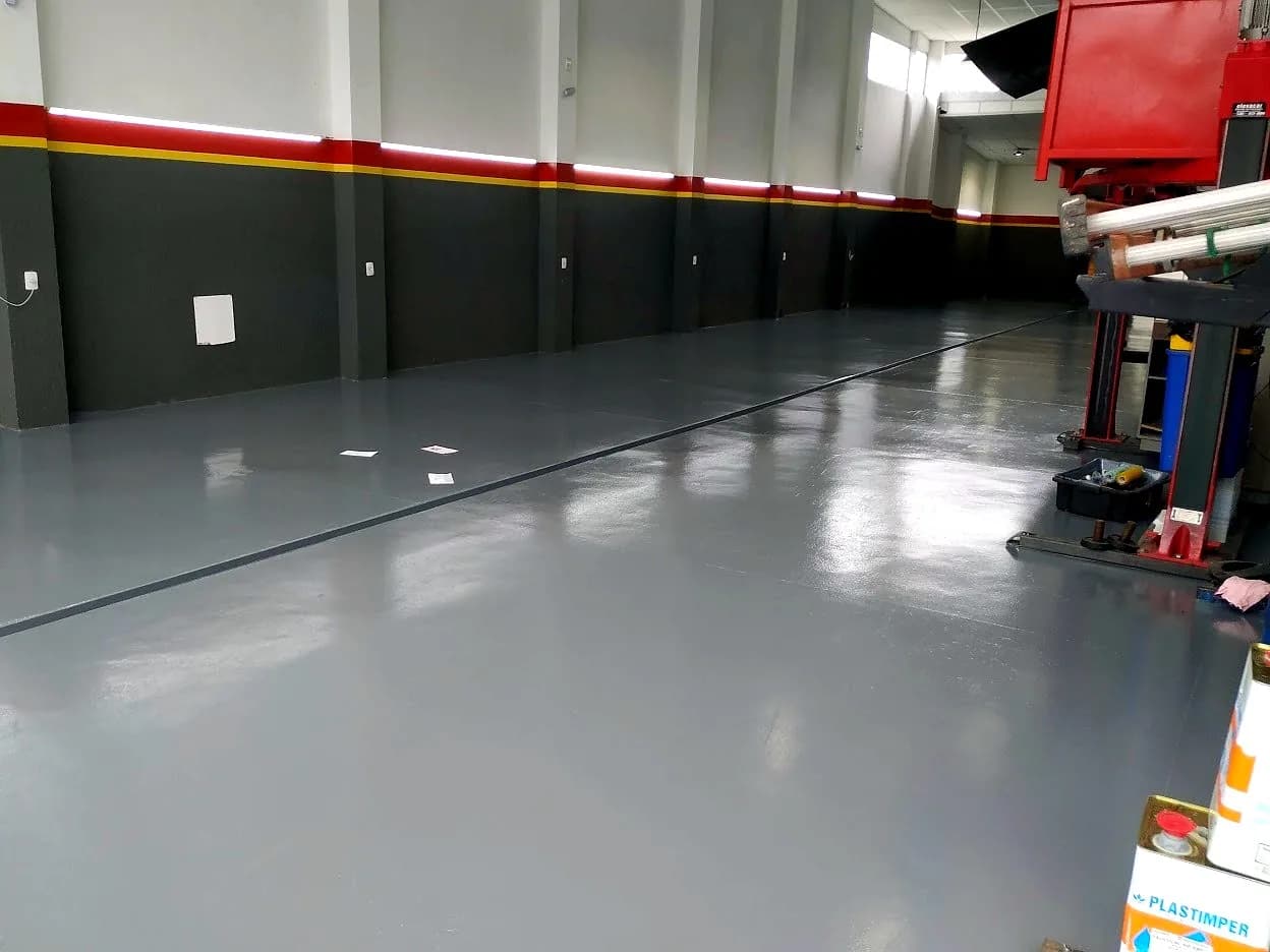 Piso epóxi cinza em galpão industrial com sinalização de faixas